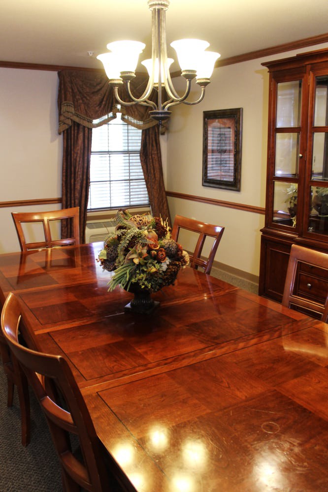 A traditional dining room with a wooden table, chairs, and a chandelier, featuring a floral centerpiece.