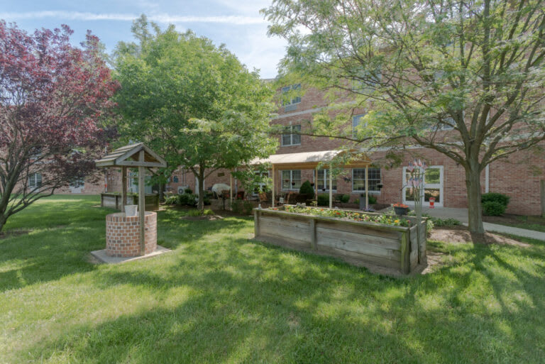 A serene garden with lush greenery and a brick building in the background.