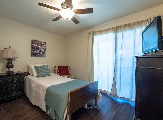 A cozy bedroom with a single bed, ceiling fan, and wooden flooring.