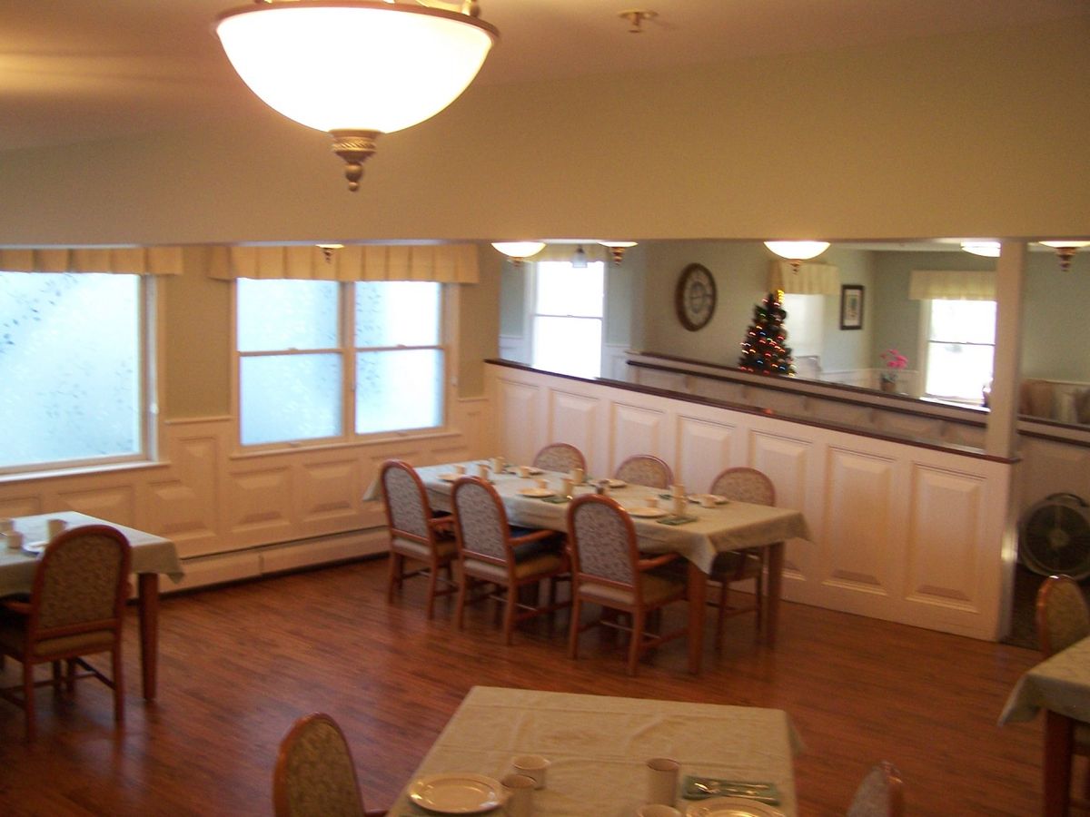 A cozy dining room setup with tables and chairs, featuring soft lighting and wooden flooring.