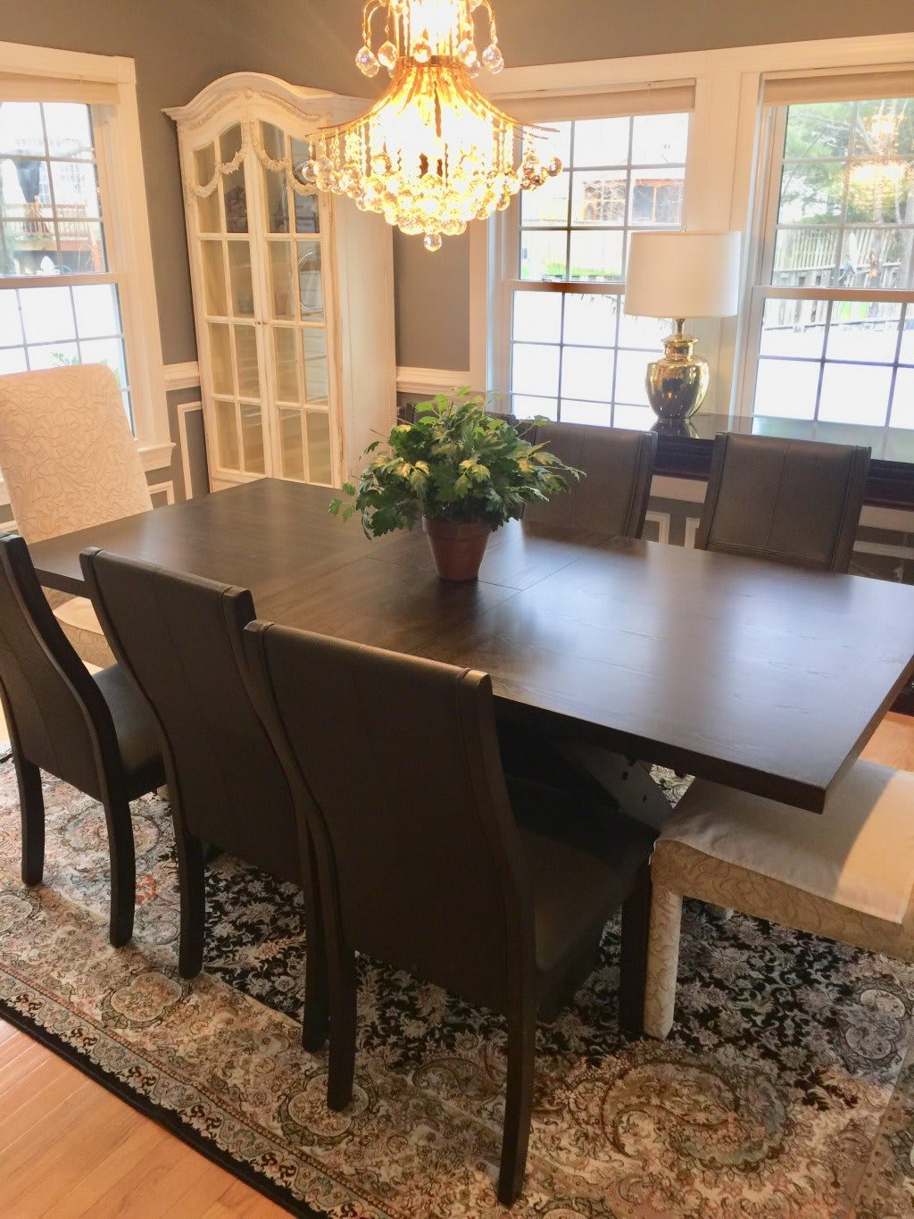 A well-furnished dining room featuring a large wooden table with chairs, a decorative chandelier, and natural lighting from the windows.