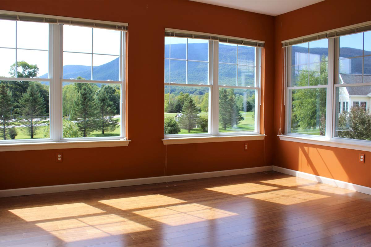 An empty room with large windows offering a scenic mountain view and sunlight streaming in.