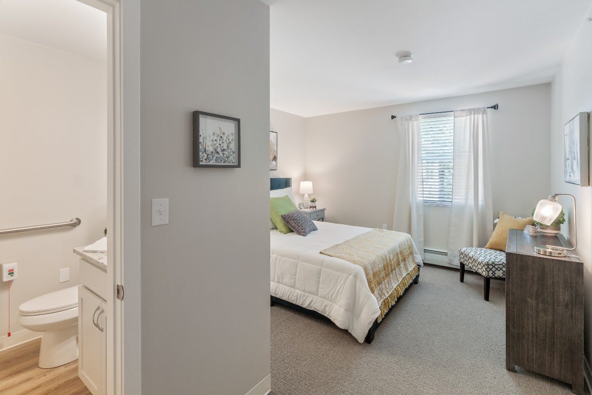 A cozy bedroom with a neatly made bed, soft lighting, and a window providing natural light.