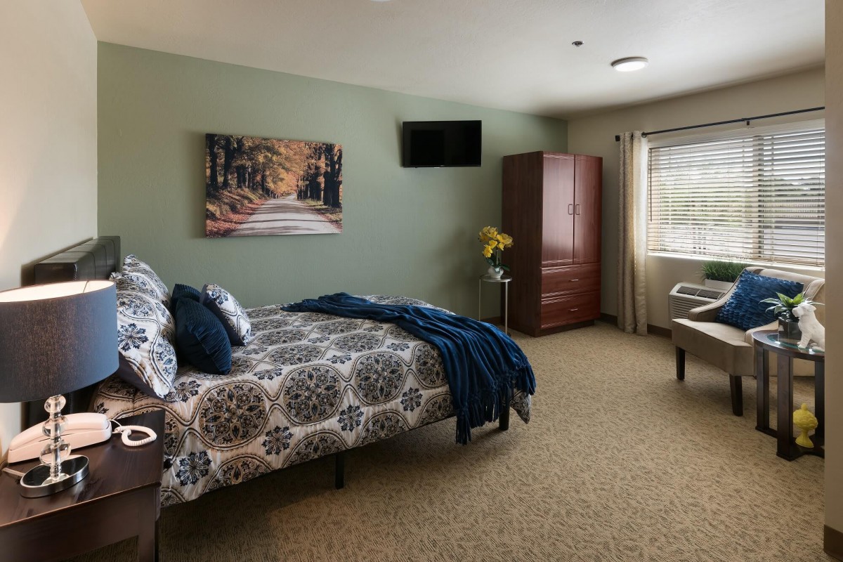 A cozy bedroom with patterned bedding, an armoire, and a wall-mounted TV.