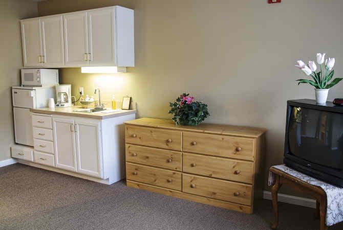 A cozy room with a wooden dresser, kitchenette, and flower arrangement.