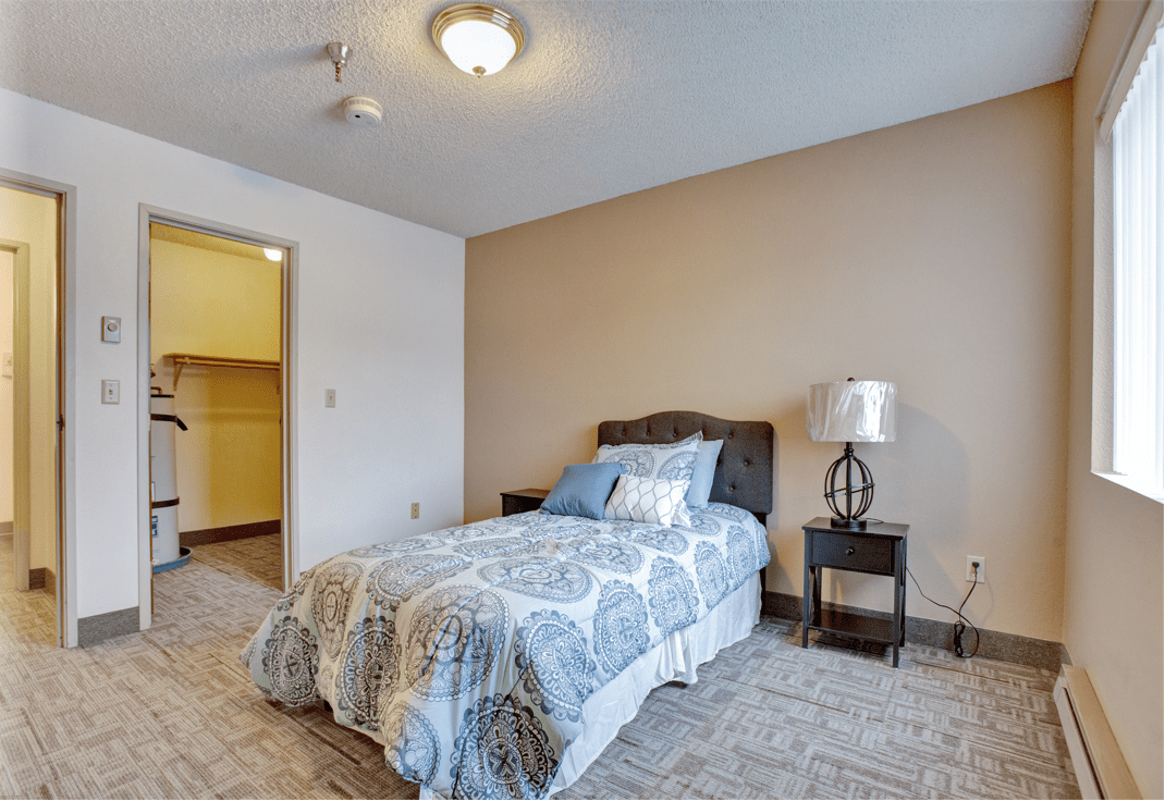 A cozy bedroom with a single bed and a nightstand, featuring neutral tones and simple decor.