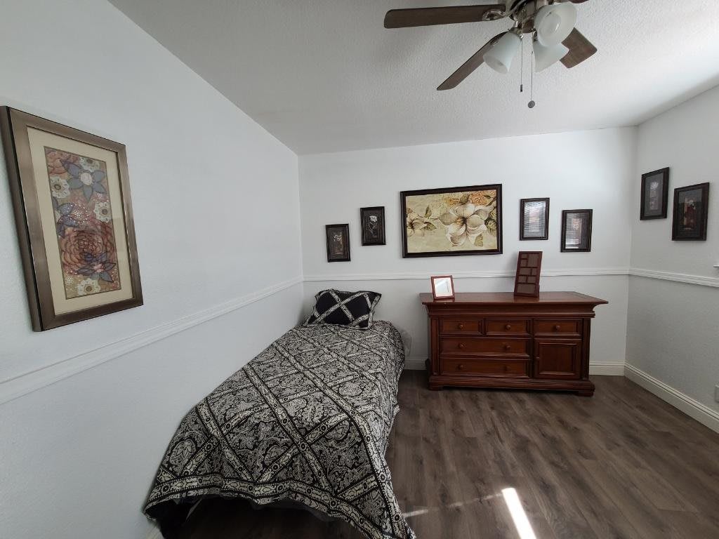 A minimalist bedroom featuring a single bed and wooden dresser with framed artwork on the walls.