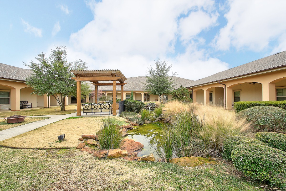 A beautifully landscaped outdoor area featuring a pergola and a small pond surrounded by lush greenery.