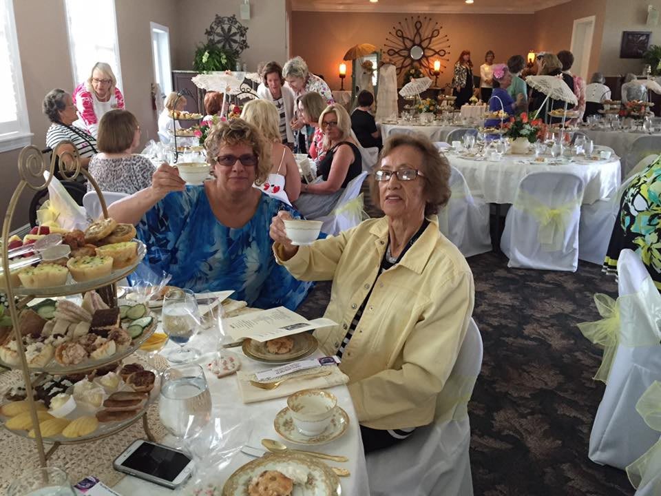 A group of people enjoying an afternoon tea party, with tables set for a gathering.
