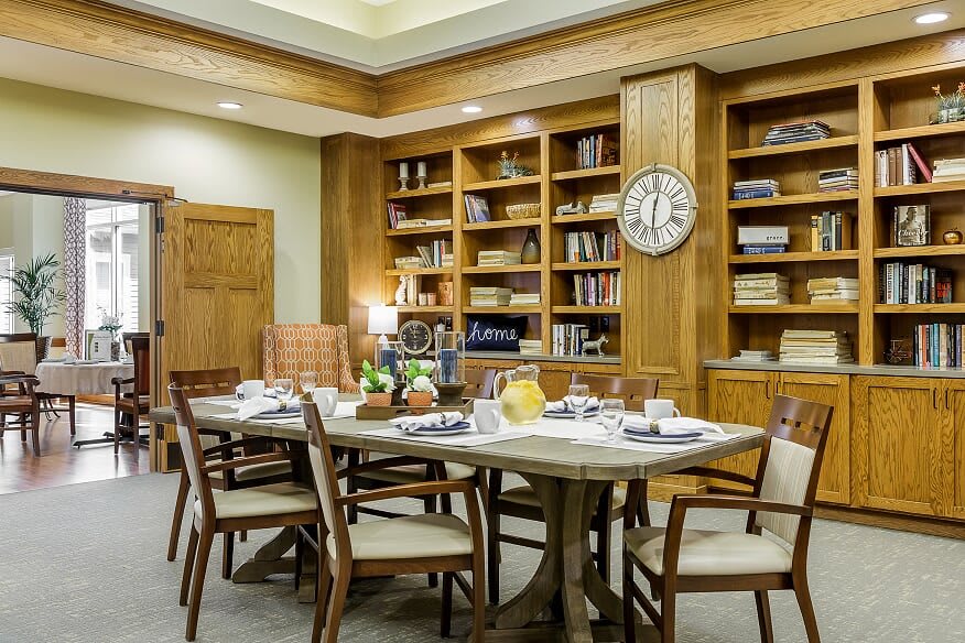 A cozy dining room with a library ambiance, featuring wooden bookshelves and a neatly set dining table.