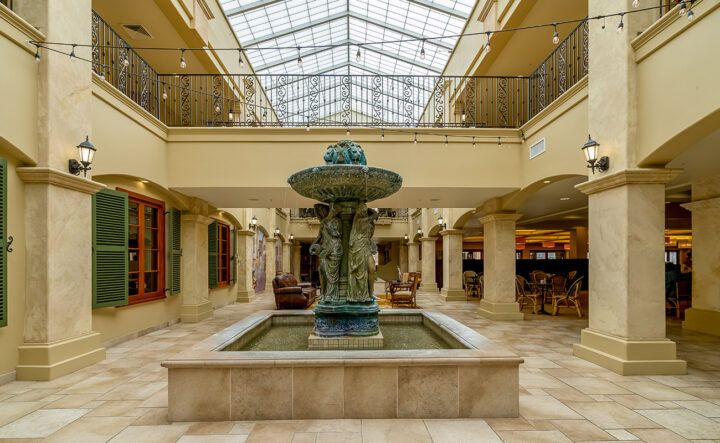 A spacious indoor atrium with a decorative fountain under a glass skylight.