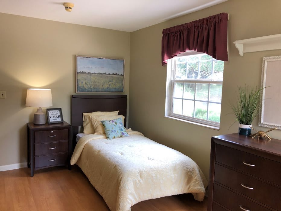 A cozy bedroom with a single bed, dresser, and a window letting in natural light.