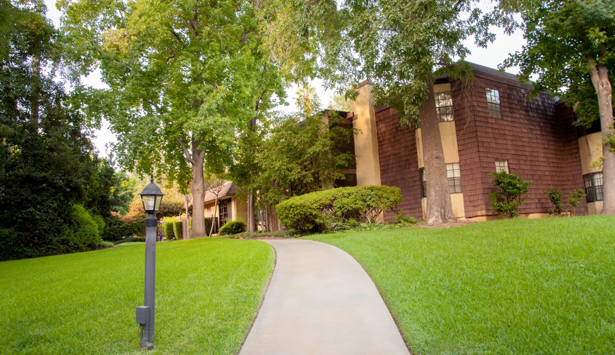 A scenic view of a pathway leading to an apartment building surrounded by lush greenery and trees.