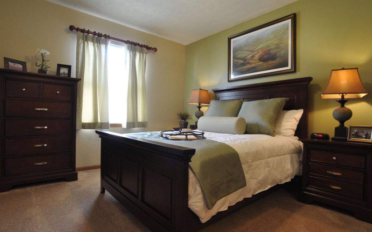 A cozy bedroom with neatly arranged bedding, a bedside lamp, and artwork on the wall.