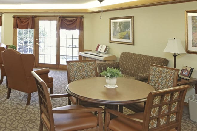 A cozy living room with a round table, chairs, couch, and a piano near large windows.