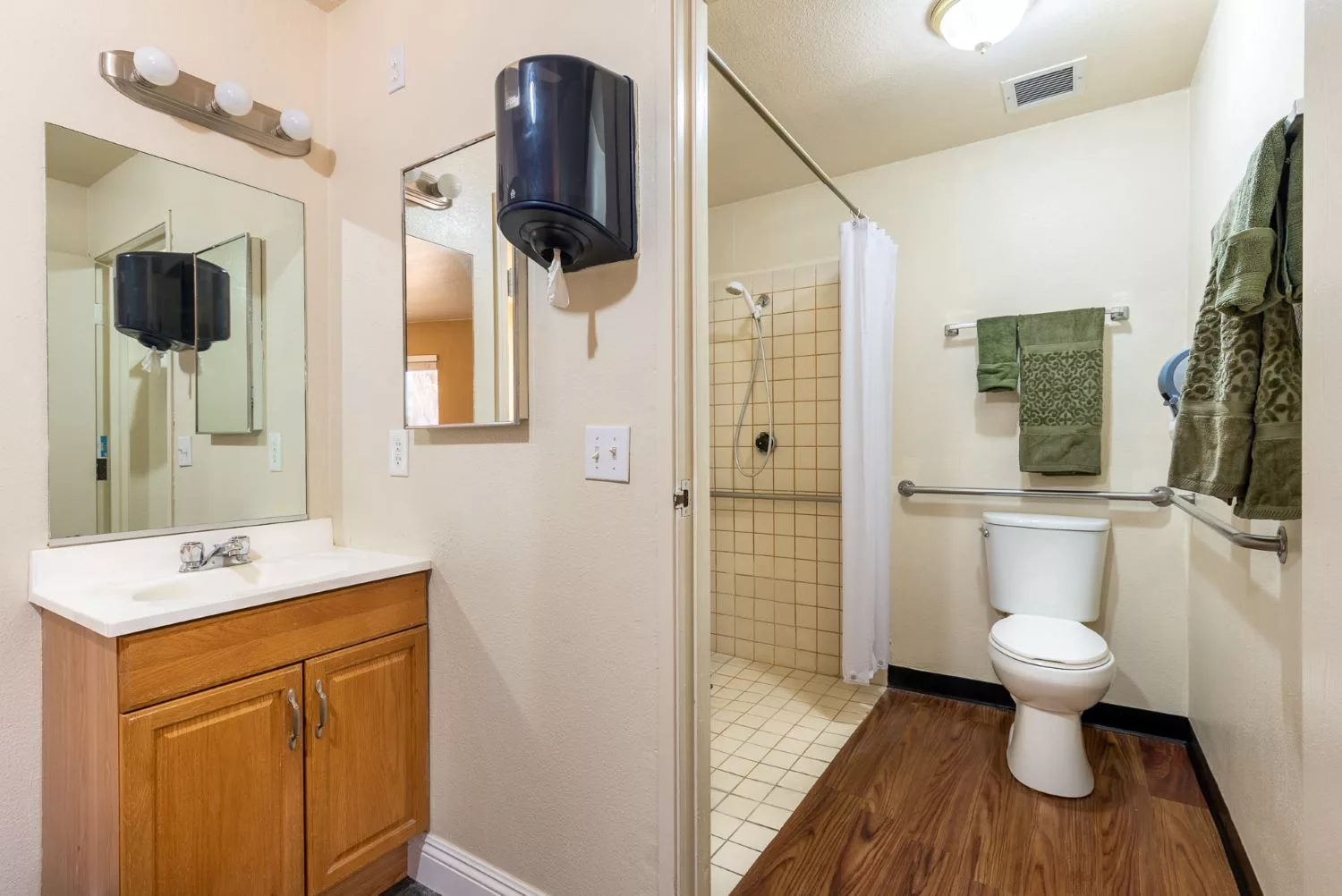 A clean and accessible bathroom featuring a shower, toilet, sink, and mirror.