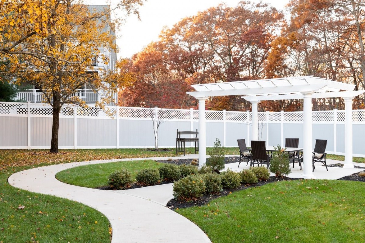 A beautifully landscaped garden featuring a pergola with outdoor seating, surrounded by autumn foliage.