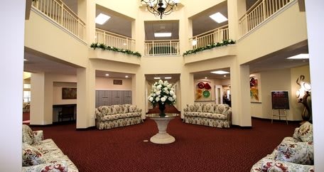A spacious and elegantly decorated lobby area featuring a central floral arrangement, comfortable seating, and a chandelier.
