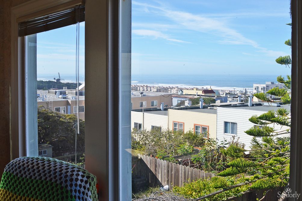 A scenic urban view from a window, showcasing residential buildings and a glimpse of the ocean under a clear blue sky.