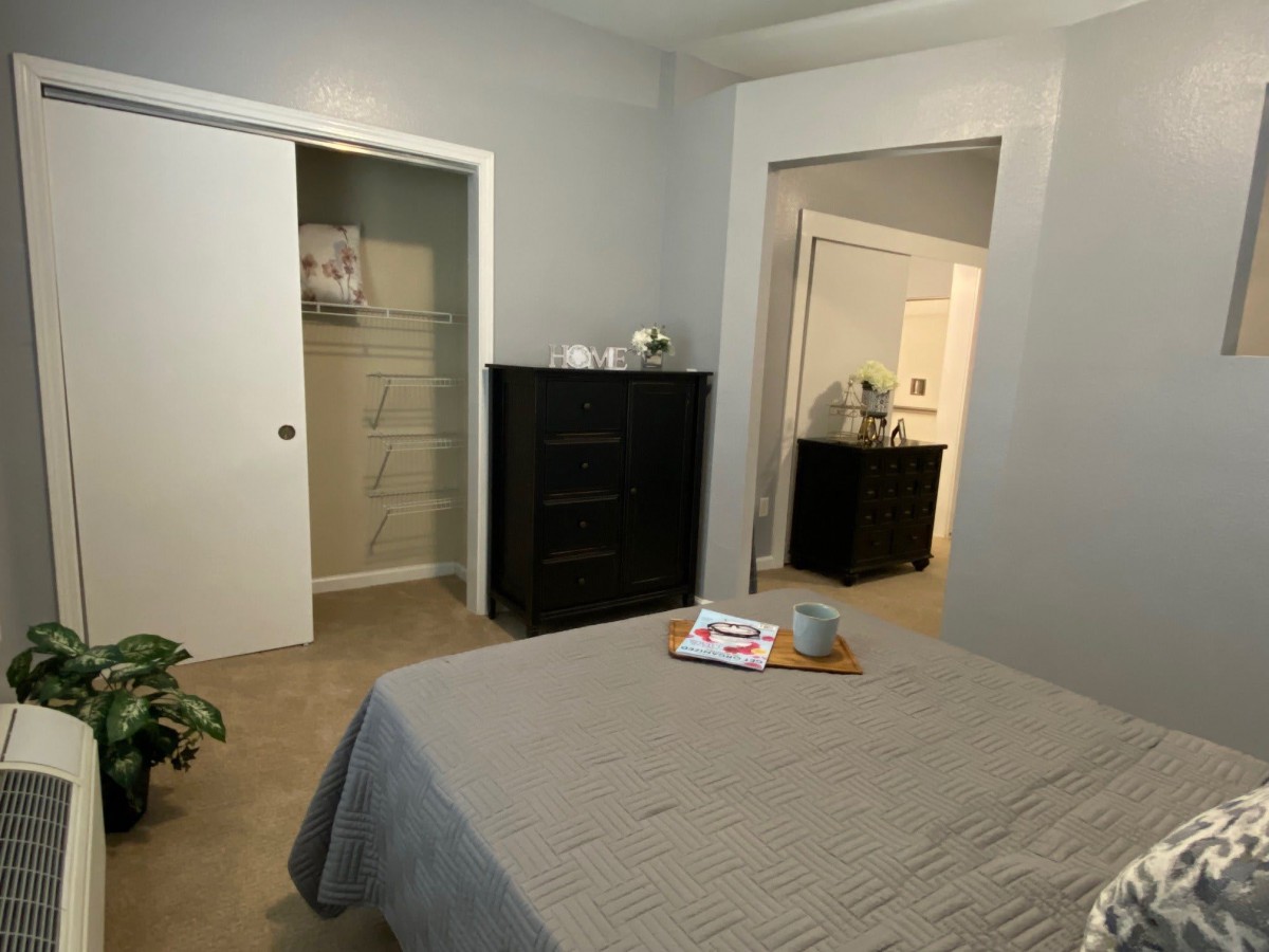 A minimalist bedroom with a neatly made bed, dresser, and open closet.