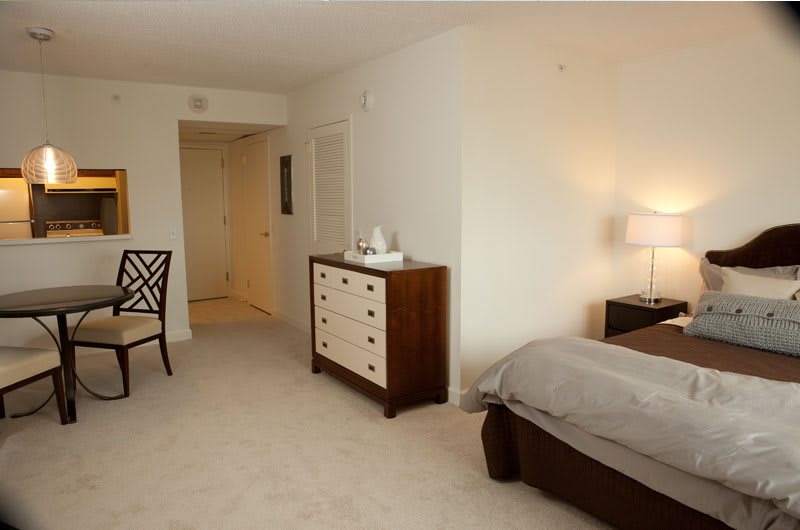 A cozy bedroom with a bed, dresser, and chair, featuring soft lighting.