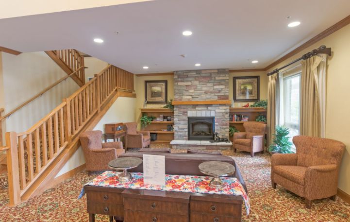 A cozy living room featuring a stone fireplace, comfortable seating, and wooden staircase.
