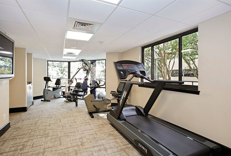 A bright and spacious gym with various exercise equipment, including treadmills and stationary bikes.