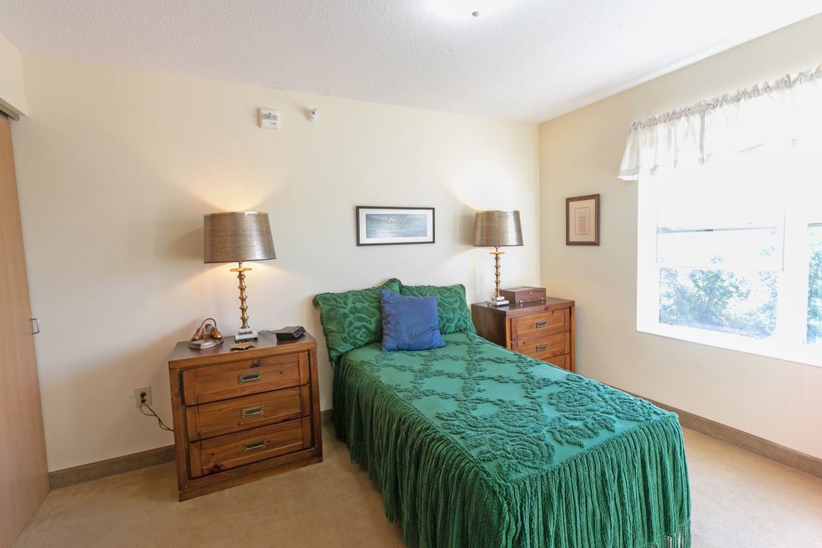A cozy bedroom with a single bed adorned with green bedding, flanked by wooden nightstands and table lamps.