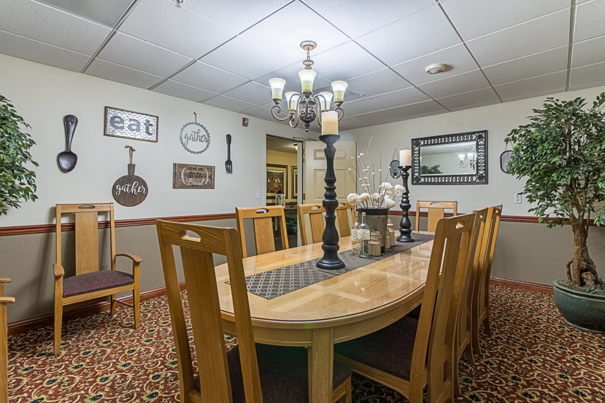 A cozy dining room featuring a large wooden table surrounded by chairs, adorned with a chandelier and decorative wall art.