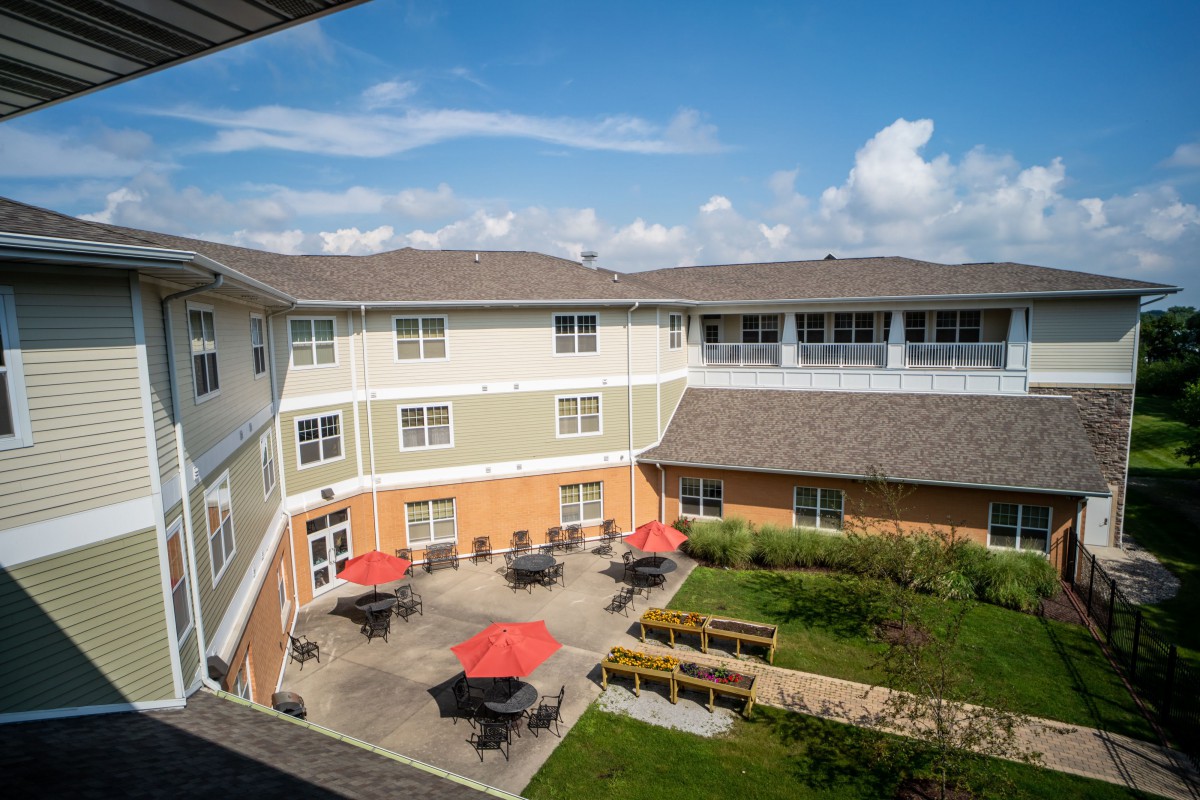 A view of a multi-story building with a spacious courtyard featuring patio furniture and red umbrellas under a clear sky.