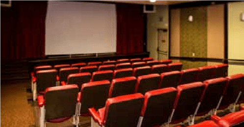 An empty cinema theater with red seats facing a large screen.