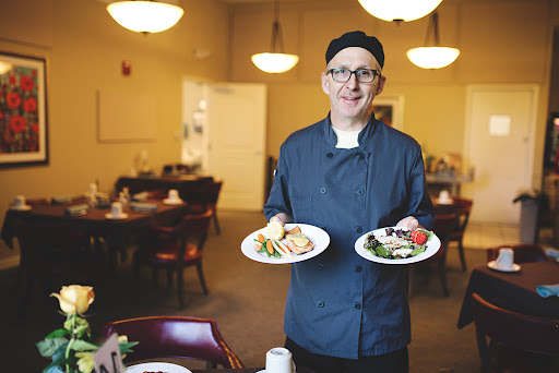 A chef proudly presenting two beautifully arranged plates of food in a cozy restaurant setting.