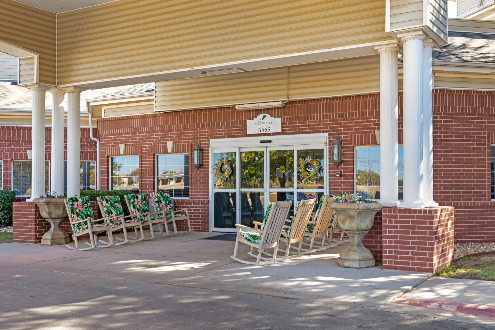 A building entrance with multiple rocking chairs lined up outside.