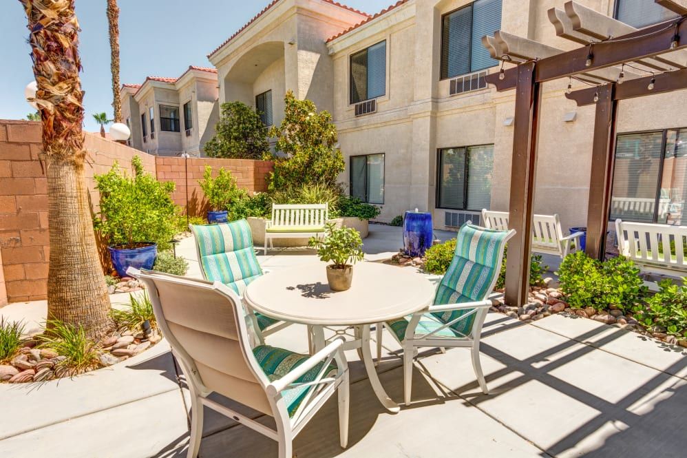 A sunny outdoor patio area with a table and chairs surrounded by greenery.