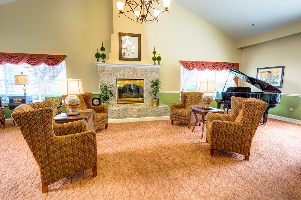 A cozy living room with a fireplace and comfortable seating, featuring elegant decor and a grand piano.