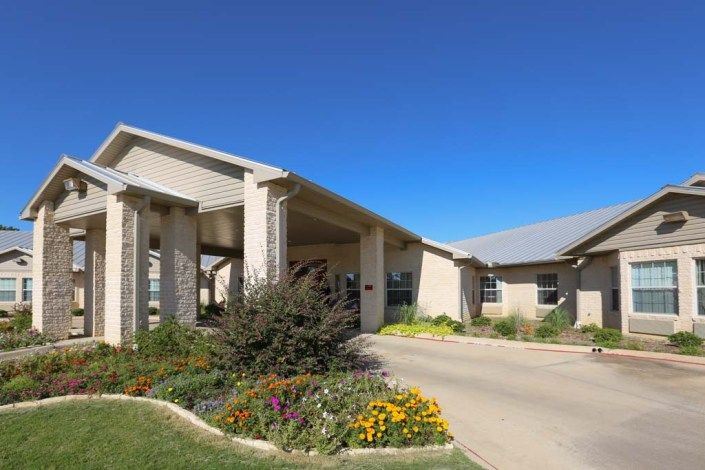 A modern residential building surrounded by landscaped gardens and a clear blue sky.