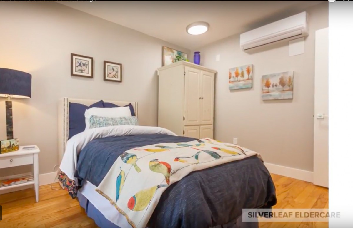 A cozy bedroom featuring a single bed with colorful bedding, wall art, and an air conditioning unit.