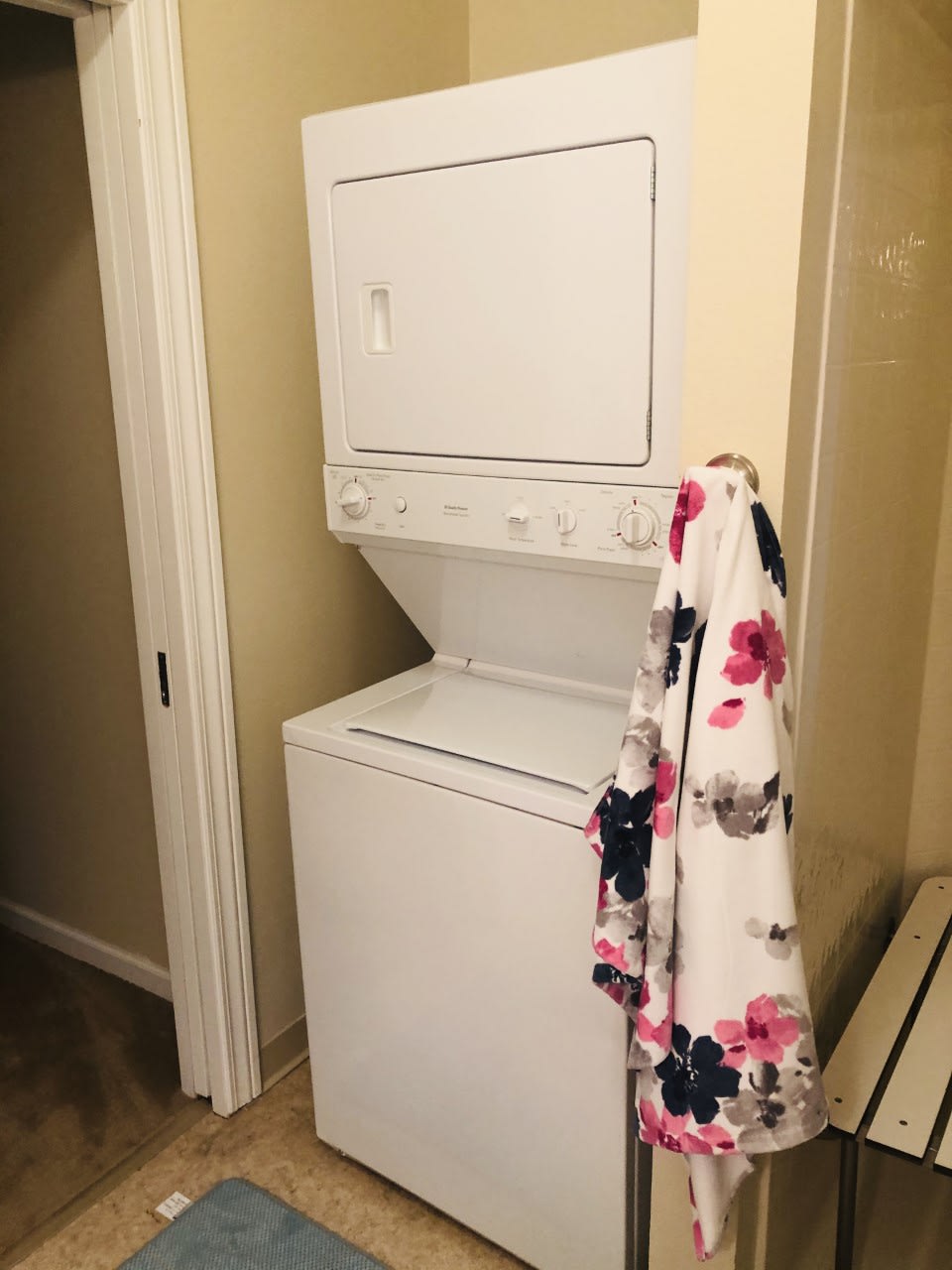 A compact stacked washer and dryer unit in a small laundry space with a floral cloth hanging on the side.