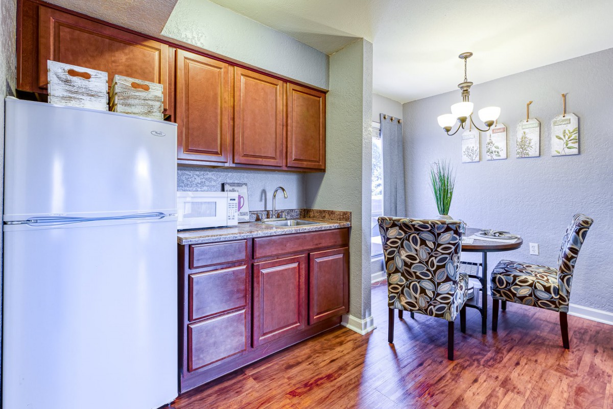 A cozy kitchen and dining area with wood cabinetry, a refrigerator, microwave, and decorative chairs around a dining table.