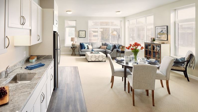 A modern living room with an open floor plan, featuring a dining area and comfortable seating in bright natural light.