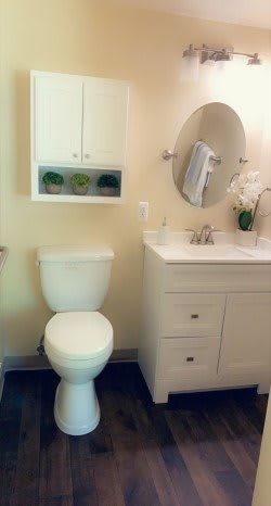 A clean and simple bathroom with a toilet, sink, mirror, and cabinet.