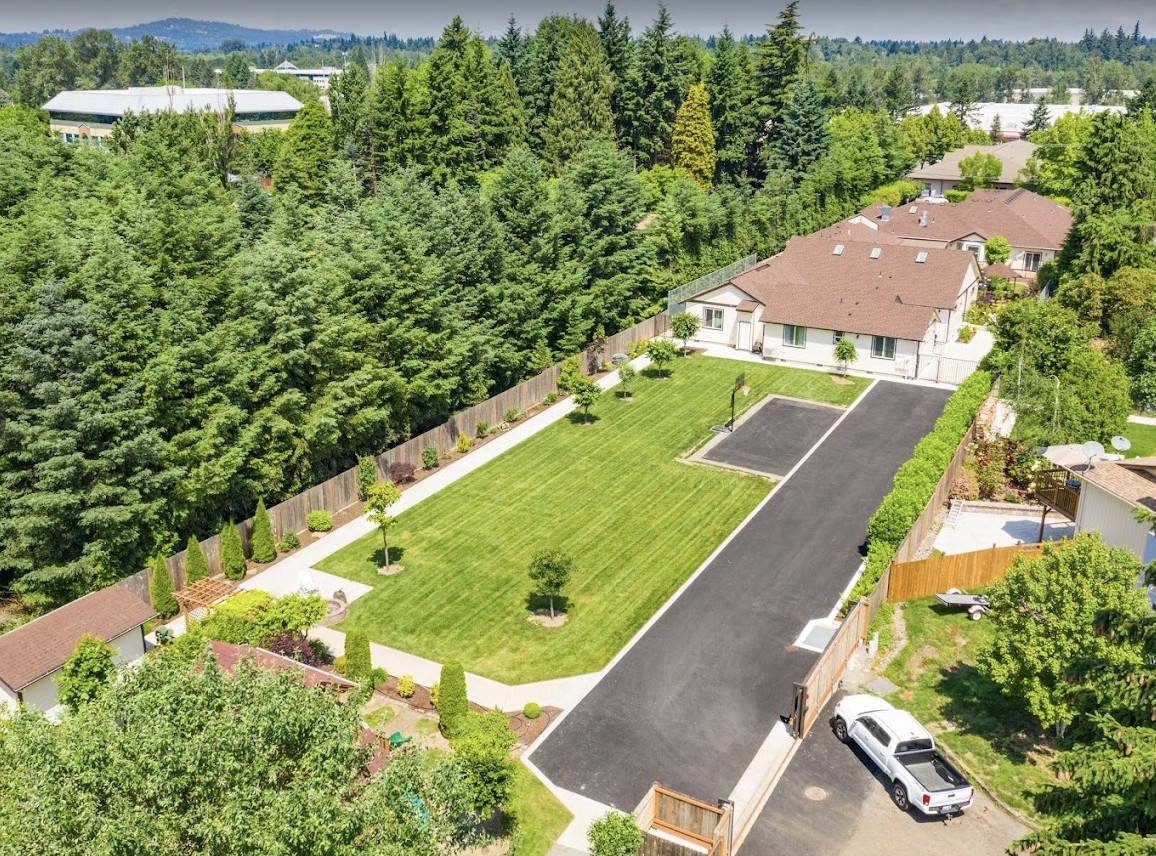 An aerial view of a residential property with a house, lawn, and surrounding greenery.