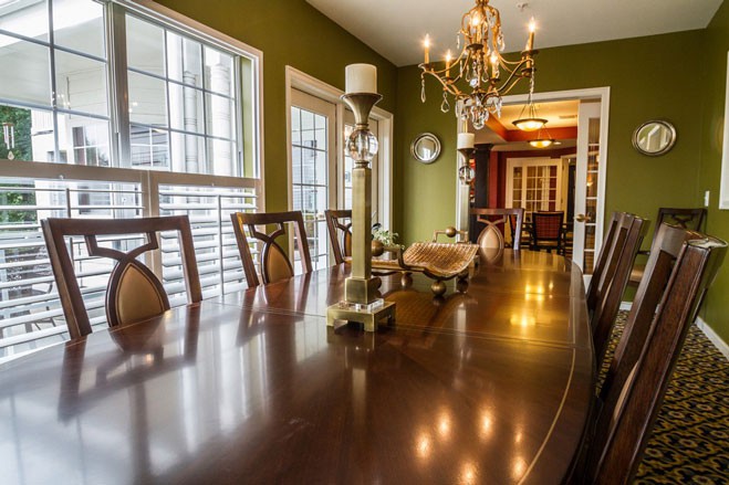 A well-lit dining room featuring a long wooden table, elegant chandelier, and green walls.