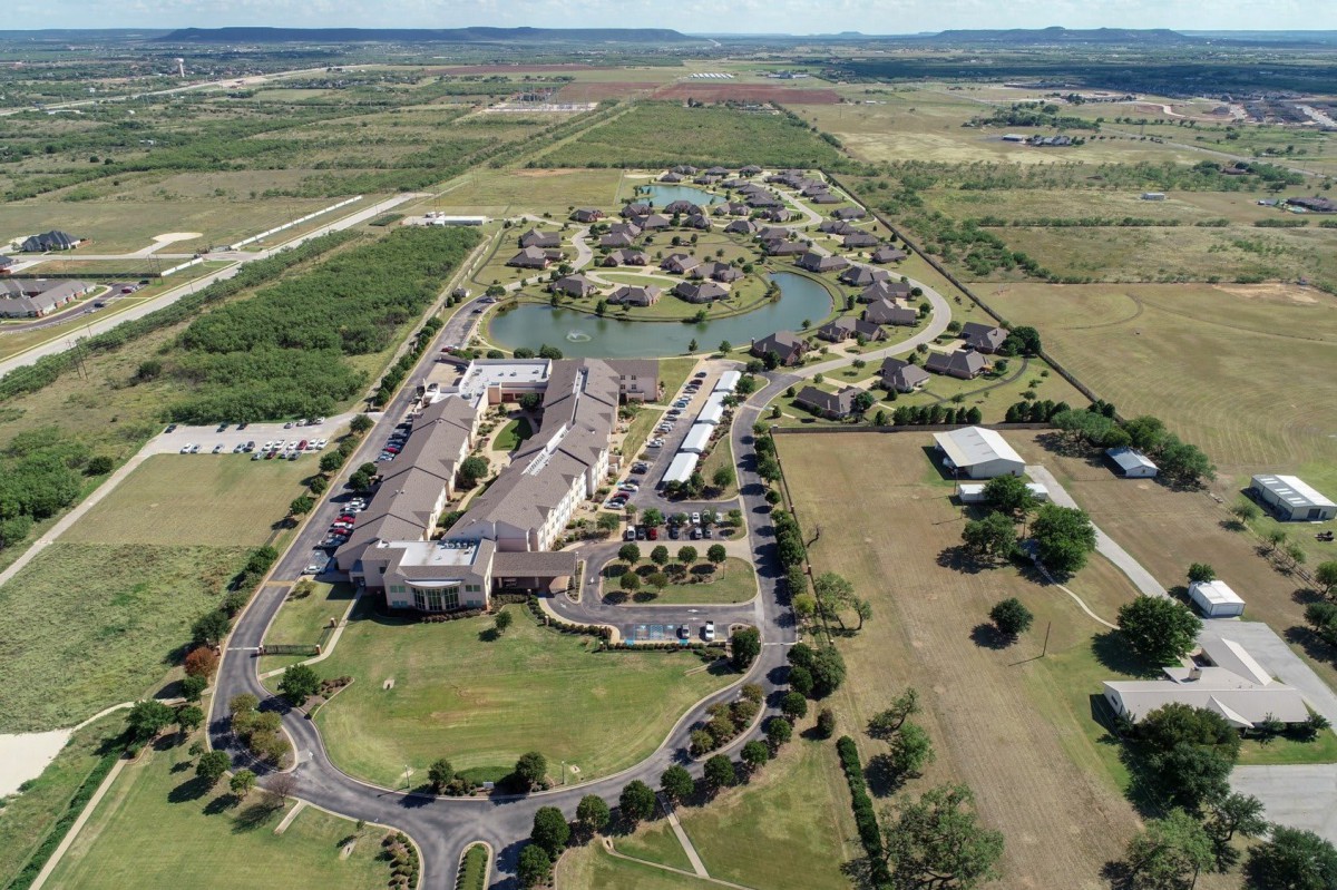 Aerial view of a large building complex surrounded by green fields and roads in the countryside.