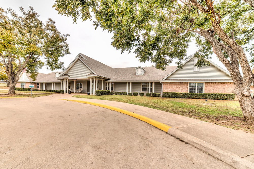 A spacious building with a large driveway and surrounding trees.