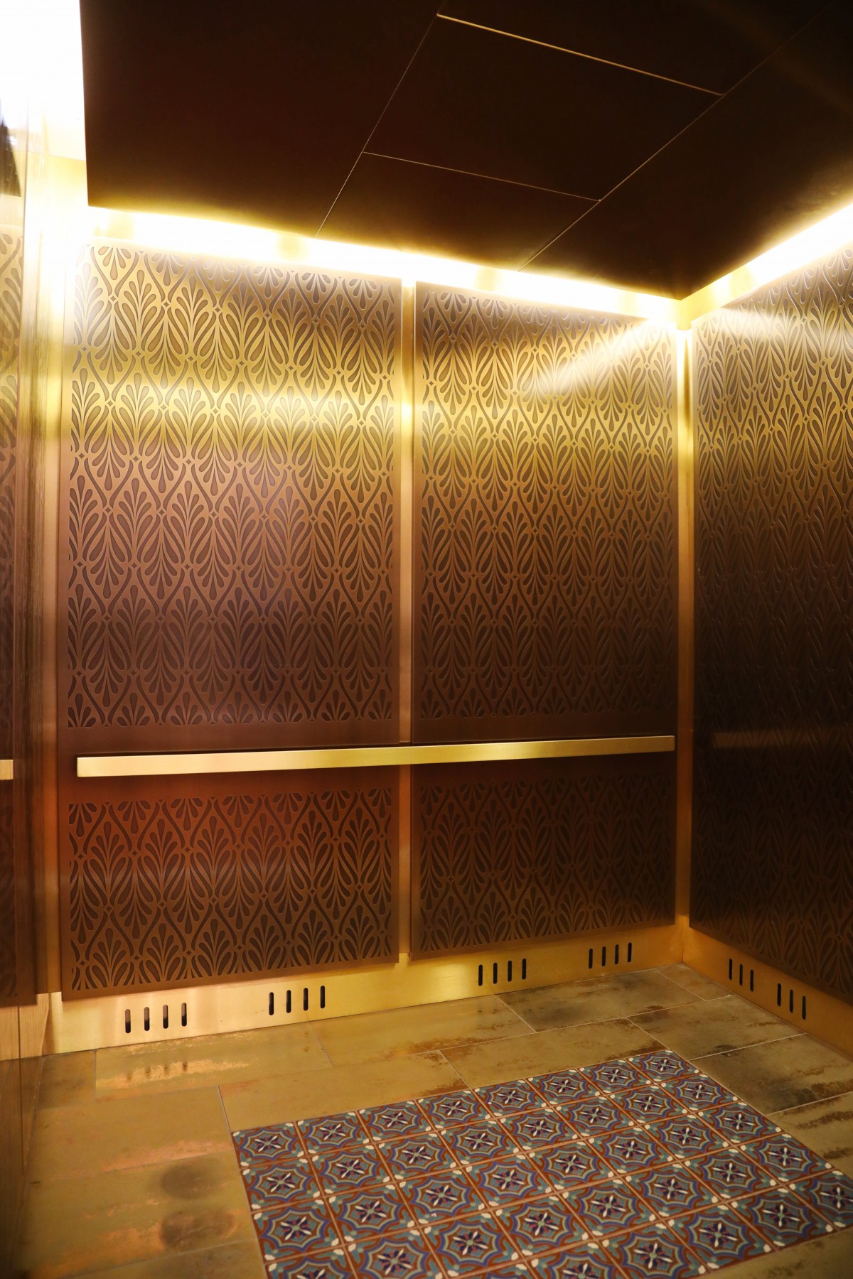Luxurious gold-toned elevator interior with bright lighting.