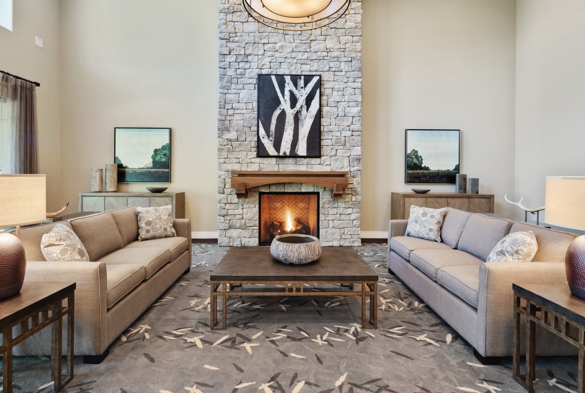 A modern living room features a central fireplace with stone walls, flanked by two gray sofas and complemented by contemporary artwork.