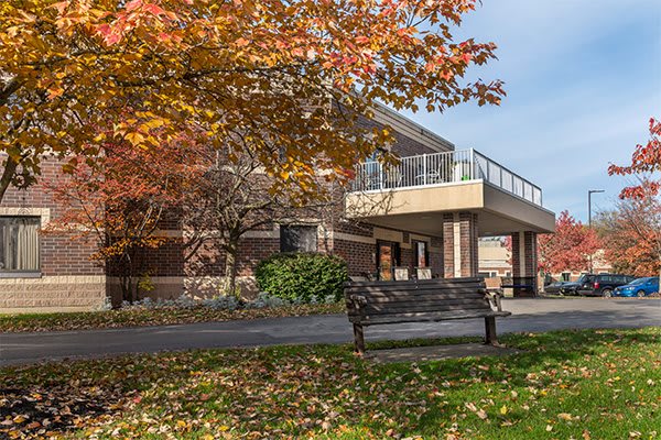 A building surrounded by autumn foliage with a bench in the foreground.