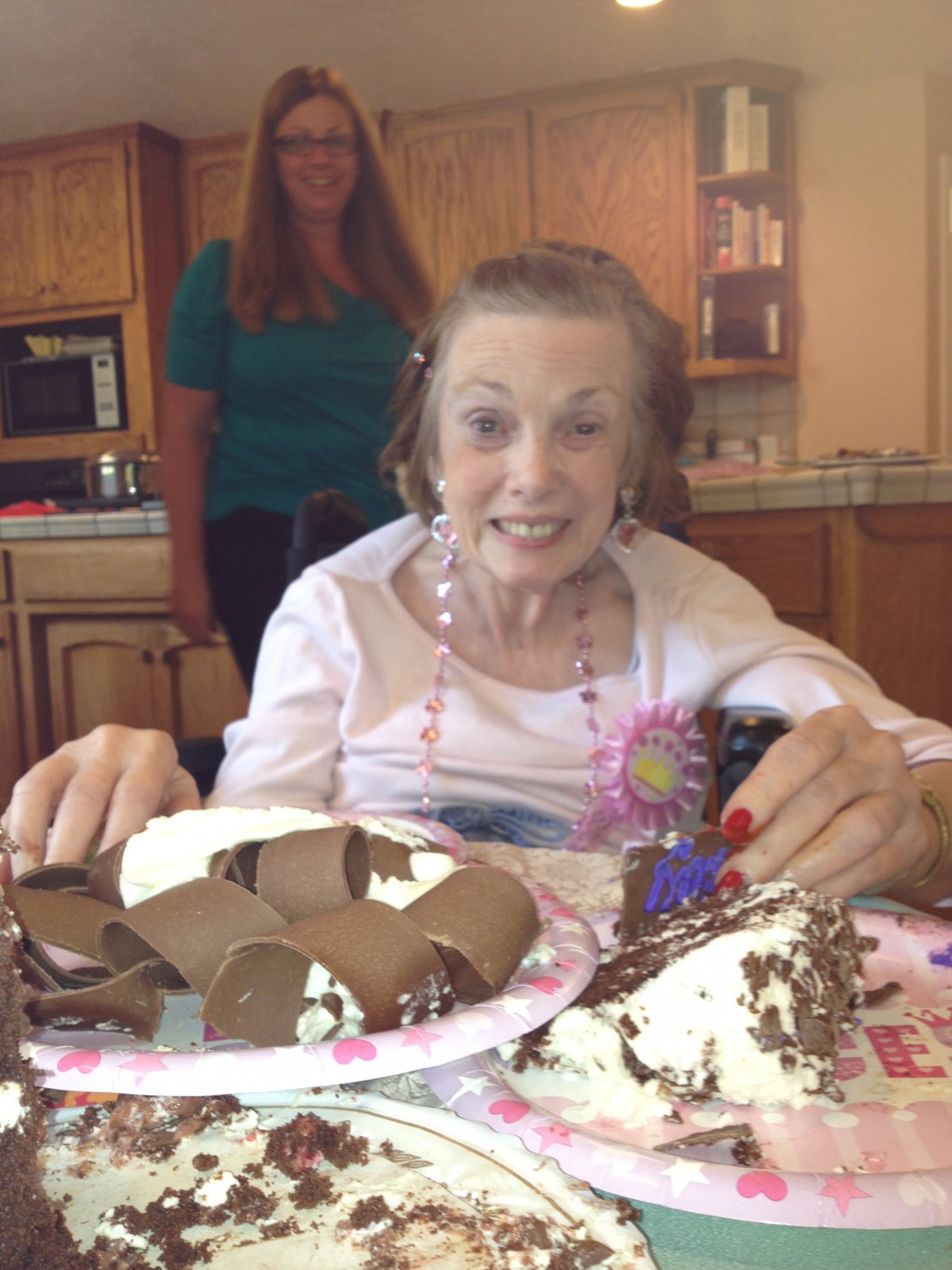 An elderly woman smiling and sitting in front of a birthday cake.