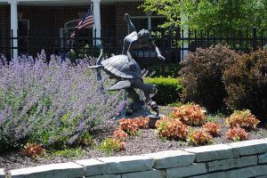 A garden sculpture depicting a child standing on a turtle surrounded by colorful plants and flowers.